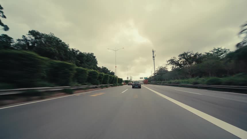 Point-of-view shot following a car driving down a lush, green highway under a dramatic, cloudy sky