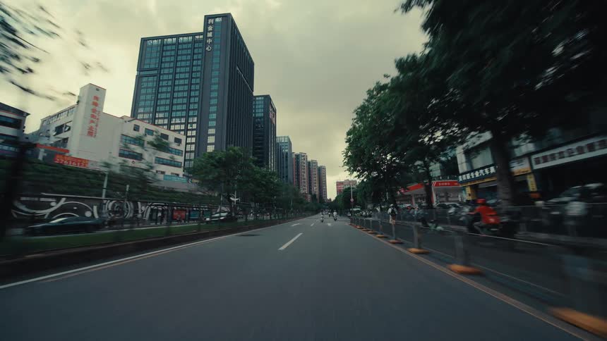 A dynamic first-person point-of-view drive emerging from under an overpass onto a wide street in a modern Asian city