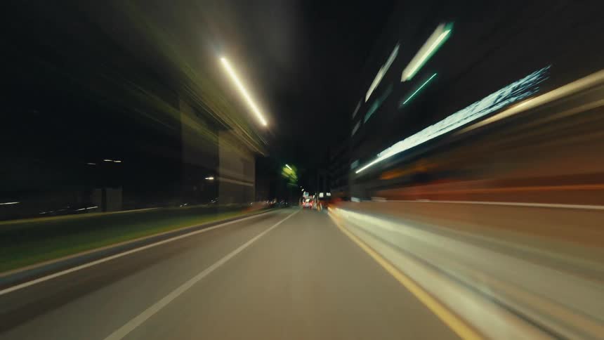 An exhilarating first-person perspective hyper-lapse of driving through a city at night with blurred light trails