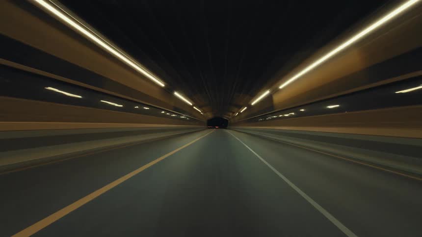 A futuristic point-of-view time-lapse captures a high-speed drive through brightly lit highway tunnels at night