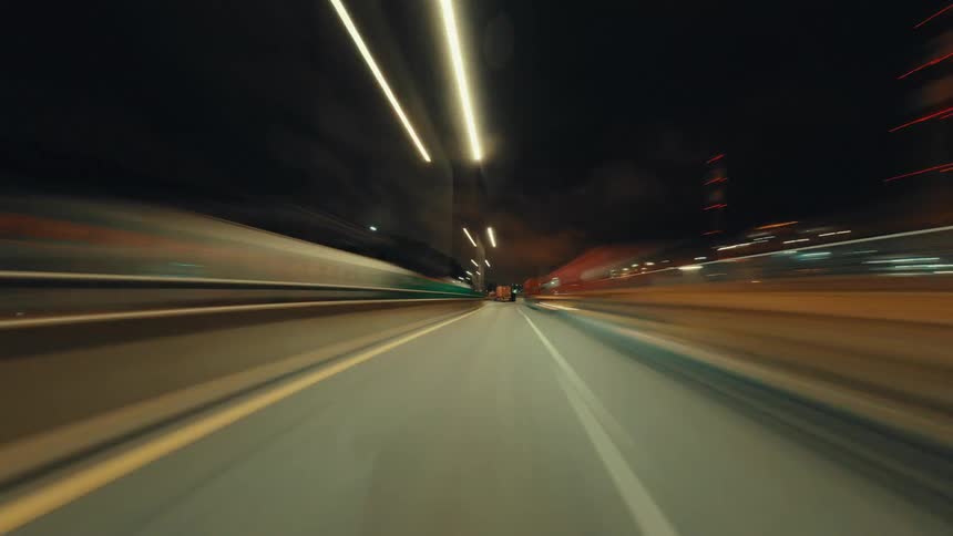 Mesmerizing hyper-lapse captures the blur of city lights while driving down an empty highway at night