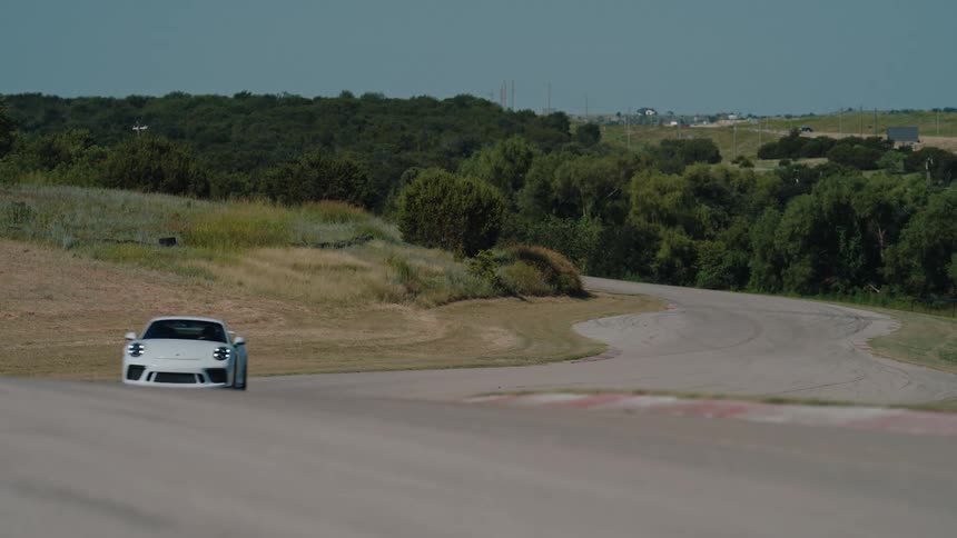 A white luxury sports car takes a turn on a countryside racetrack on a sunny day