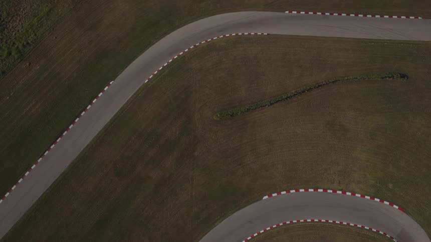 An aerial top-down view slowly rises to reveal a winding, empty racetrack surrounded by lush green grass
