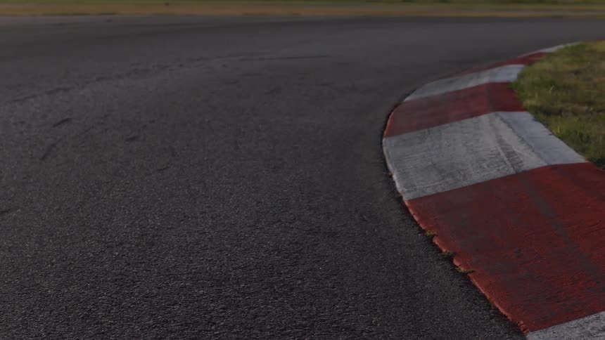 Close-up, static shot of a racetrack corner with a red and white striped kerb