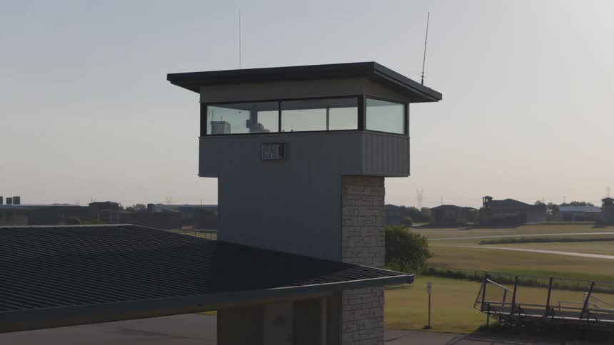 An aerial shot slowly zooms into a modern observation tower overlooking a racetrack on a hazy day