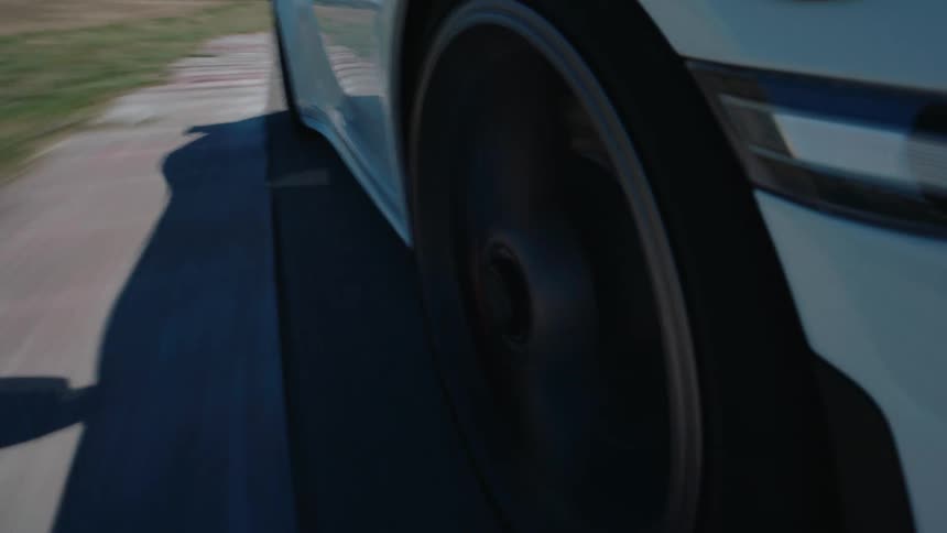 An extreme close-up shot captures a sports car's wheel spinning rapidly as it drives along a professional racetrack on a sunny day