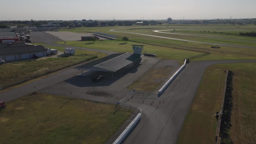 An aerial shot slowly approaches a vacant observation tower at a rural racetrack during the day