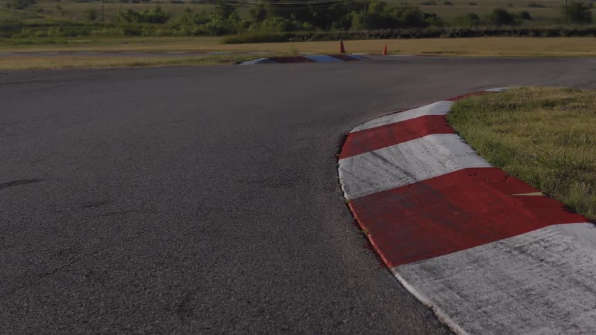 Slow dolly shot of a red and white rumble strip on the corner of an empty racetrack