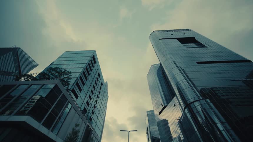 A low-angle perspective moves through a modern cityscape, revealing towering glass skyscrapers and passing under a changing traffic light