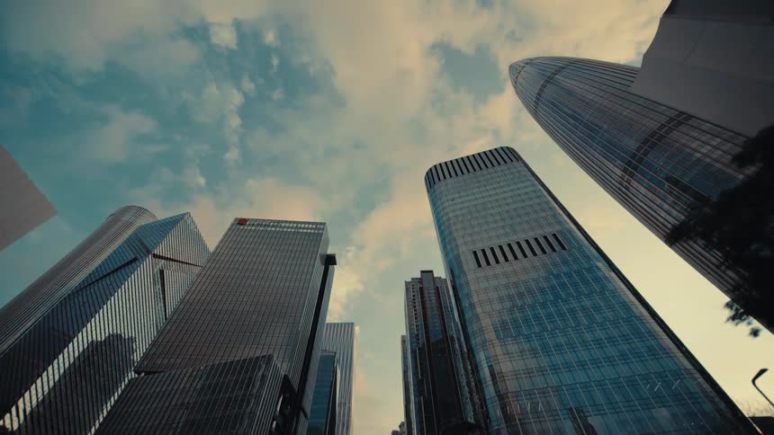 A dramatic opening reveal of towering modern skyscrapers in a city, filmed from a low-angle perspective while moving slowly forward