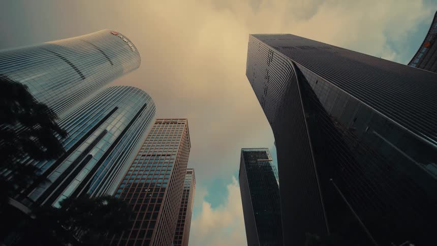 A low-angle dolly shot looking up at impressive modern glass skyscrapers while driving through a city canyon