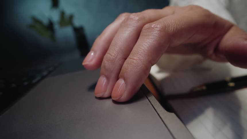 A close-up shot shows a woman's manicured hand resting and tapping on a laptop trackpad