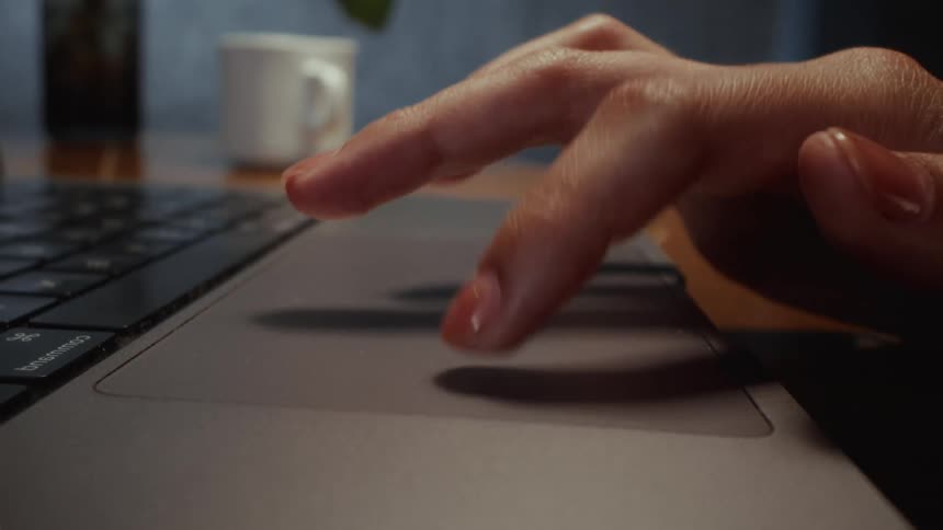 A slow-motion close-up of a person's hand with a manicure tapping on a laptop trackpad