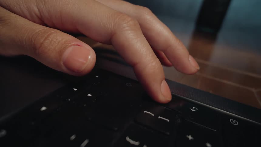 Close-up of a woman's manicured hand tapping and swiping on the touch bar of a modern laptop