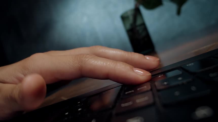 A close-up shot of a person's hand impatiently tapping their fingers on a laptop's touchpad while waiting