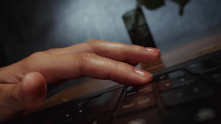 A dramatic cinemagraph shows a hand resting motionless on a laptop keyboard, deep in thought