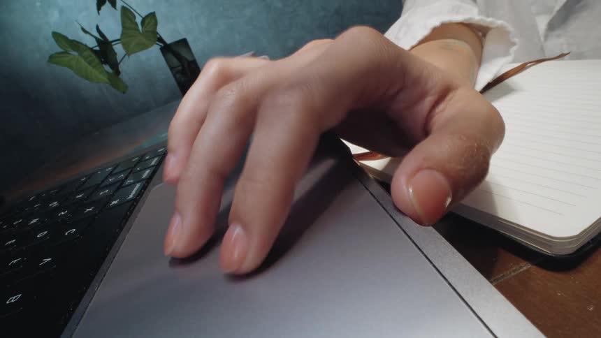 Extreme close-up of a person's hand scrolling and clicking on a laptop trackpad in a home office
