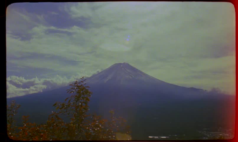 A vintage, grainy film reveals the majestic Mount Fuji in Japan under a cloudy sky