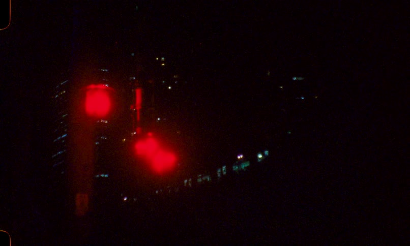 Grainy vintage footage of a red traffic light blinking against a dark city skyline at night