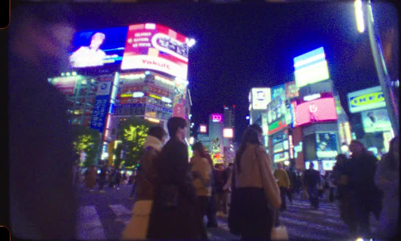 Chaotic and grainy 8mm-style footage follows a massive crowd of people walking across Tokyo's Shibuya Crossing at night amidst dazzling neon lights