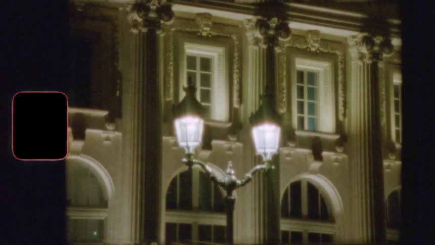 Vintage 8mm film shows an old-fashioned street lamp illuminating an ornate European building at night