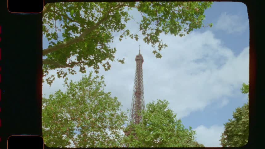 A vintage 16mm film shot shows the Eiffel Tower framed by lush green trees on a sunny day in Paris