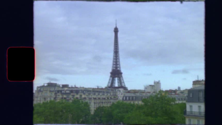 Vintage 8mm film footage pans across a Parisian cityscape to reveal the iconic Eiffel Tower on a cloudy day