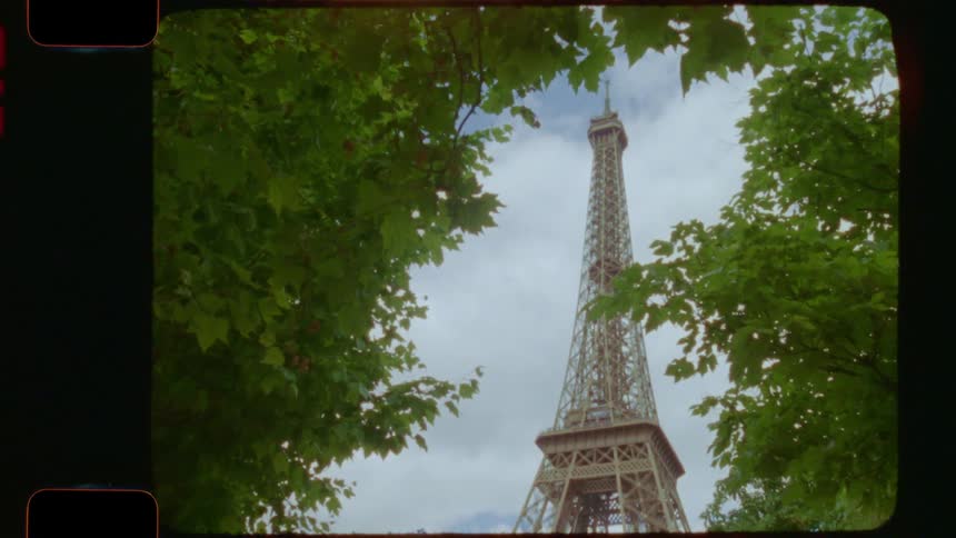 A 16mm film shot tilts up at the Eiffel Tower from a beautiful park on an overcast day in Paris, France