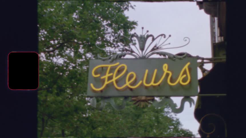 Vintage film of a charming yellow neon sign that says 'Fleurs' for a French flower shop hanging outdoors
