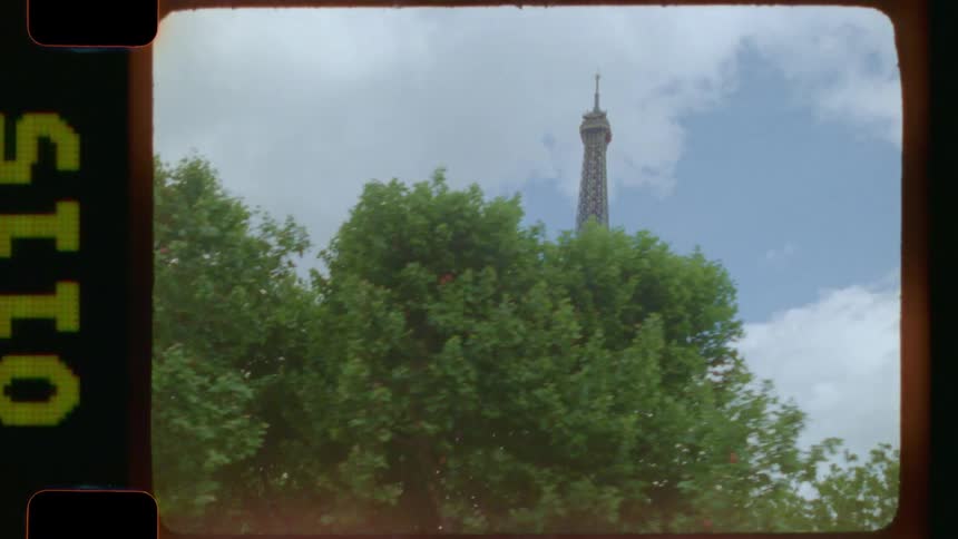 Nostalgic 16mm film captures a moving view of the Eiffel Tower through lush green trees in Paris