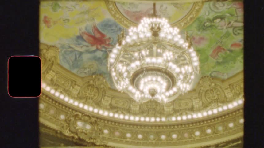 Vintage 8mm footage captures the glowing ornate chandelier and colorful painted ceiling of a grand opera house