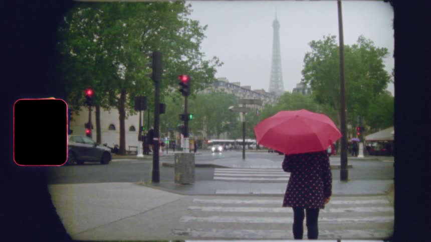 Vintage film captures a person with a red umbrella waiting at a Parisian crosswalk on a rainy day, with the Eiffel Tower in the distance