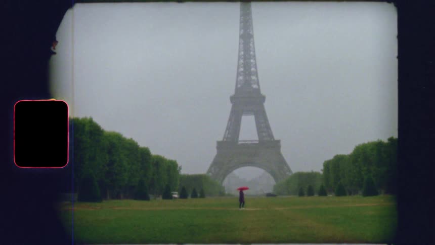 Vintage film captures a person with a red umbrella walking towards the Eiffel Tower on a foggy, rainy day in Paris