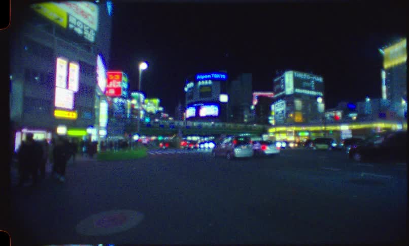 A grainy, Super 8mm style shot of a bustling Tokyo intersection at night, with glowing neon signs, pedestrians, and passing traffic