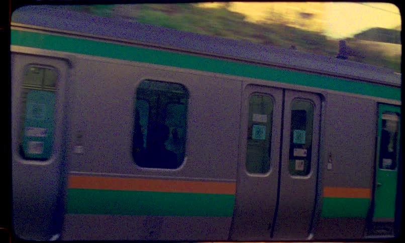 An 8mm film-style shot captures a commuter train emerging from a dark, graffiti-covered tunnel in urban Japan