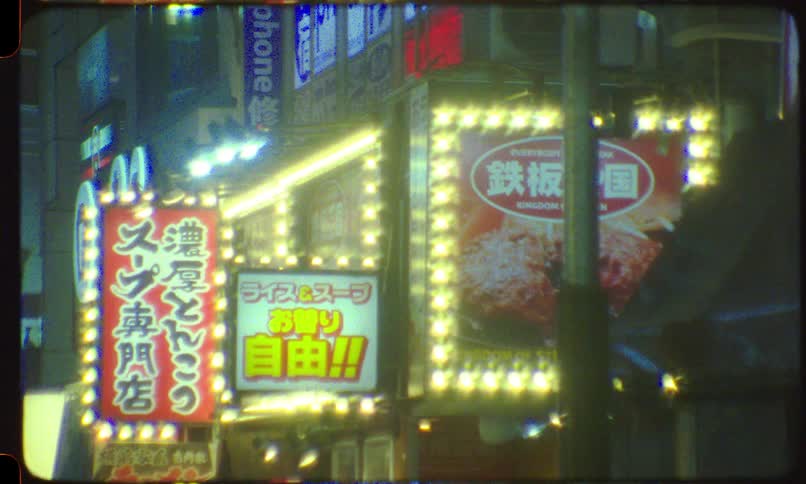 Authentic 8mm film captures the glowing neon signs and advertisements on a city street in Japan at night