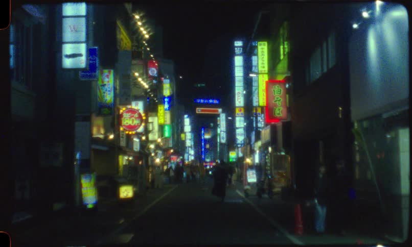 Vintage film captures a blurry, dreamlike view of a narrow Tokyo street at night, with pedestrians walking beneath a dazzling array of colorful neon signs