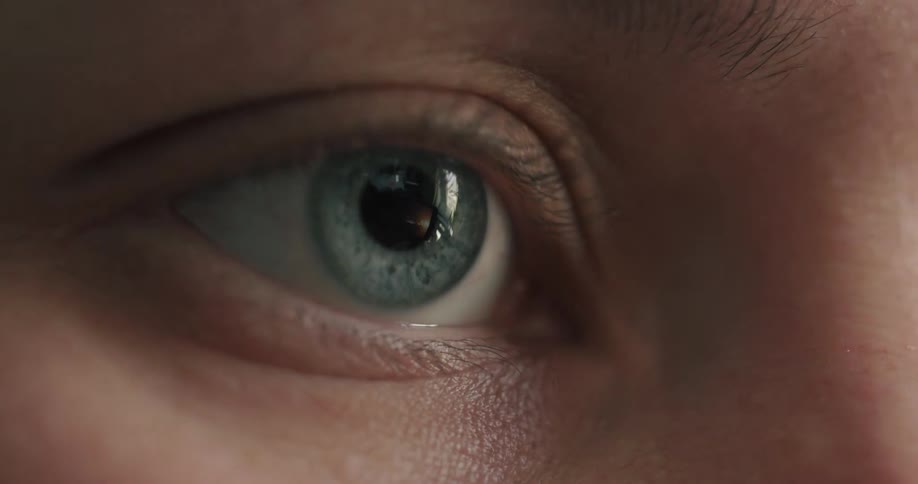 An extreme close-up on a person's blue-green eye, revealing the reflection of a screen they are watching