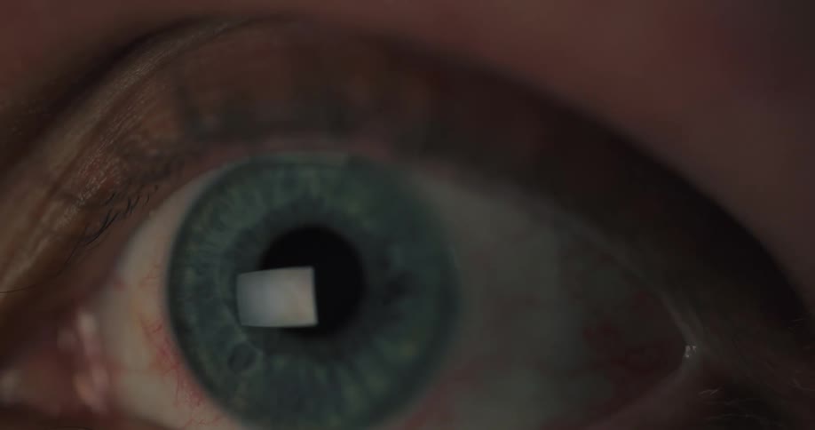 An extreme close-up of a person's eye shows the reflection of a screen as they scroll through content