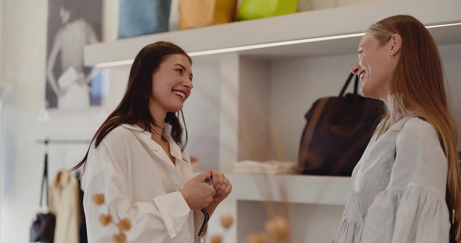 A cheerful shop assistant presents a new fragrance to a smiling female customer in a modern boutique