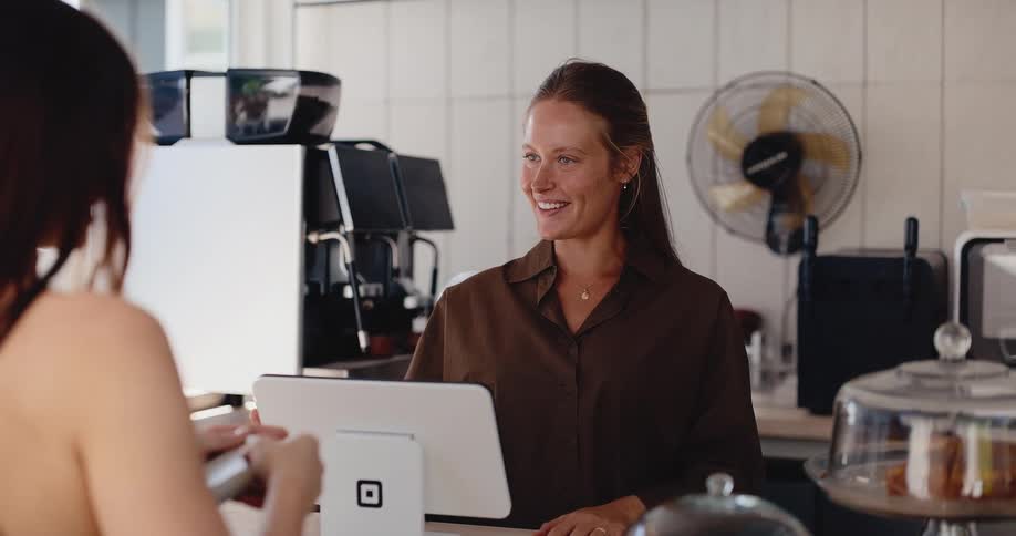 Smiling female barista assists a customer at the counter in a sunlit modern coffee shop