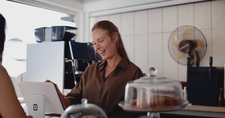 A friendly female barista smiles while taking a customer's order at the counter of a modern coffee shop