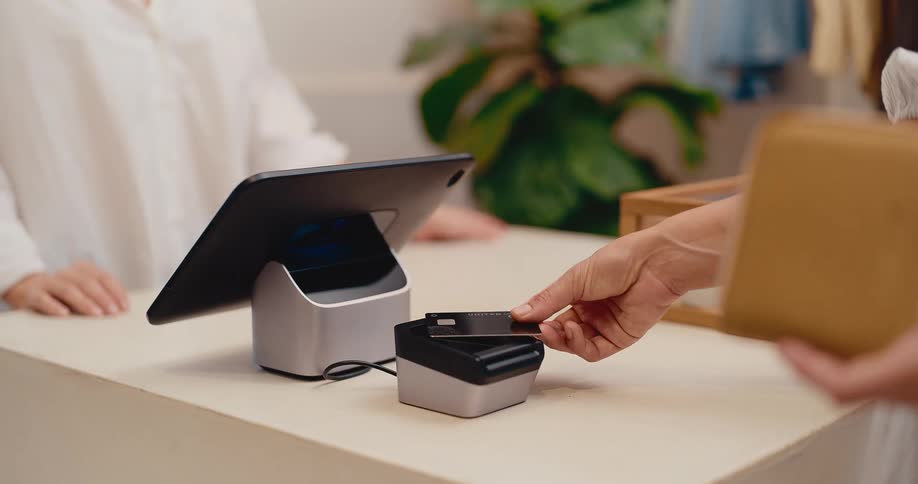Close up of a customer making a contactless payment by tapping a credit card on a reader at a modern boutique checkout counter