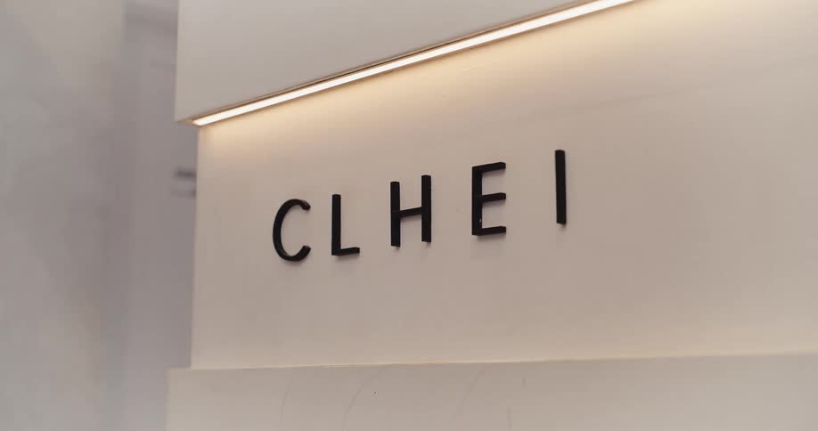A minimalist black and white sign reading 'CLHEI' is illuminated by a warm linear light