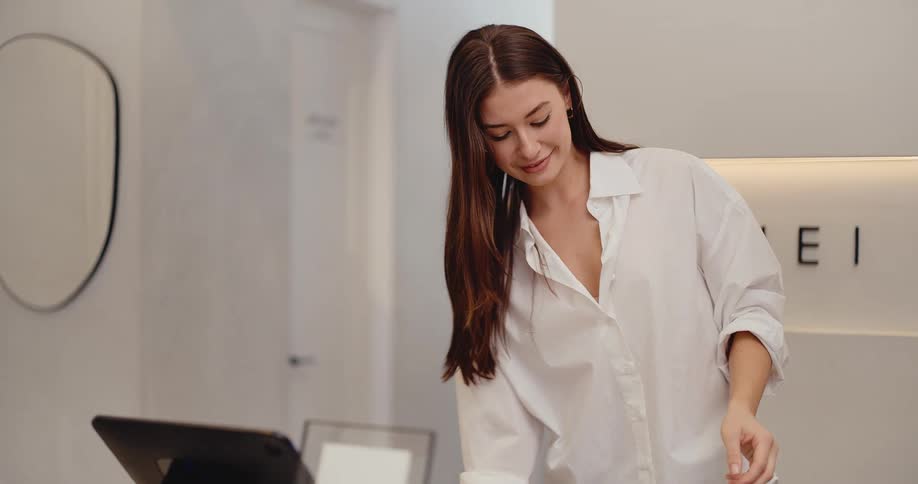 A stylish female shop assistant carefully prepares a customer's purchase, folding an item and getting a paper bag ready in a modern boutique