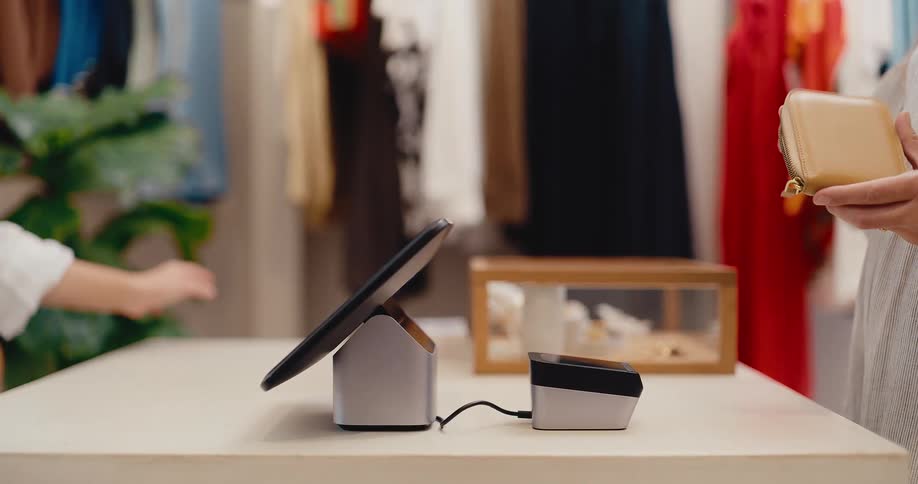 Close-up slow-motion shot of a customer tapping their credit card on a reader to complete a contactless payment in a clothing boutique