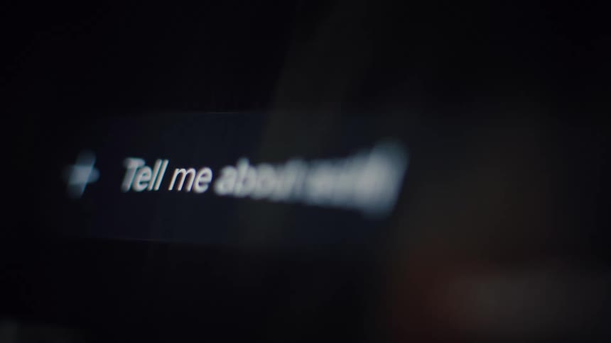 A close-up of a user typing 'Tell me about' into a search engine or AI chatbot on a dark computer screen