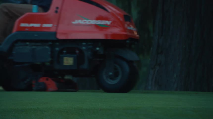 A low-angle close-up shot of a red ride-on lawn mower cutting a perfectly manicured green