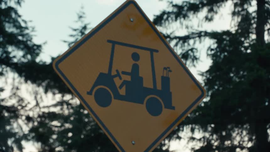 A close-up of a yellow golf cart crossing road sign with trees blurred in the background