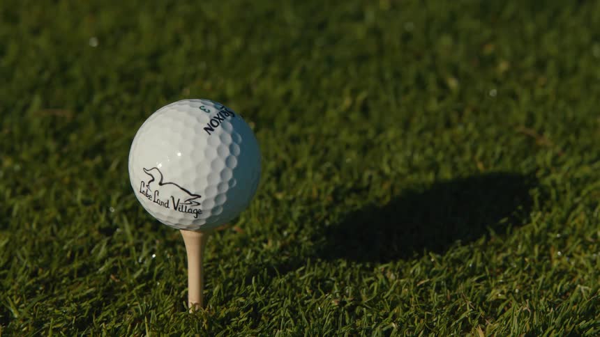 A golfer's hand carefully places a golf ball on a wooden tee in the grass in slow motion